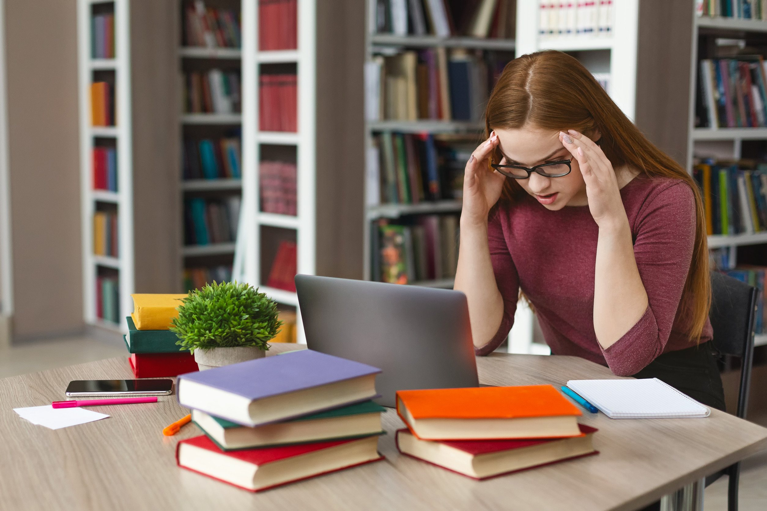 tired redhead girl sitting in front of laptop, clenching head